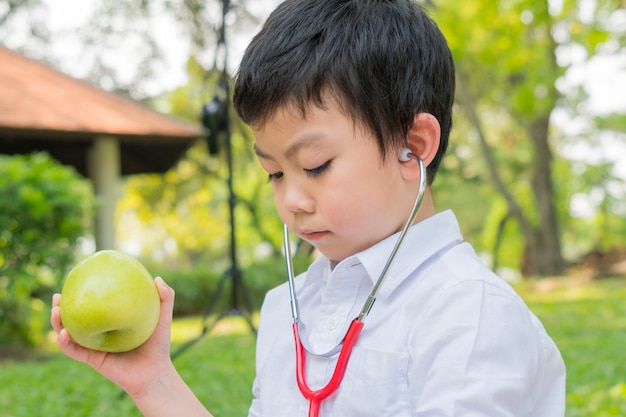 Il ragazzo usa gli stetoscopi e gioca con la mela verde della frutta