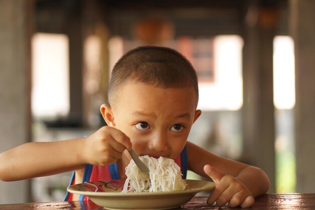 Il ragazzo usa un cucchiaio per far cadere gli spaghetti in bocca per mangiare