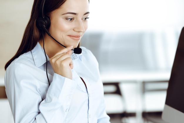 Il rappresentante del servizio clienti femminile bruna in un auricolare sta consultando i clienti online Concetto di call center e uomini d'affari