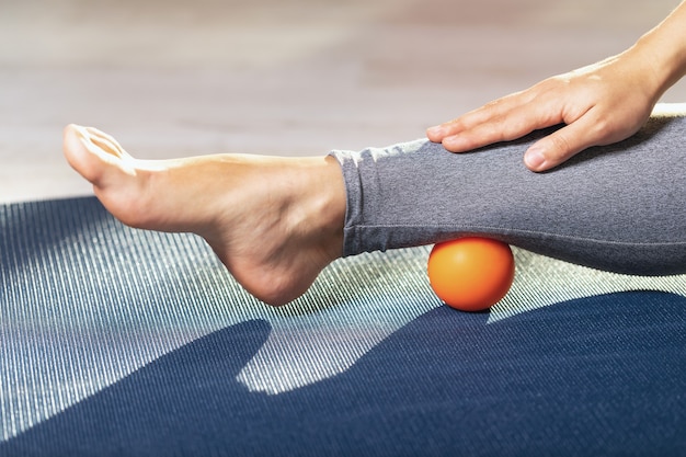 Il rilassamento miofasciale dei muscoli delle gambe con una palla da massaggio su un tappetino da ginnastica a casa previene l'affaticamento delle gambe