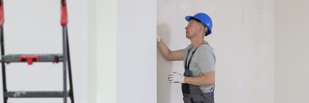 Il riparatore in elmetto controlla il problema nel concetto di riparazione e ristrutturazione della parete della casa