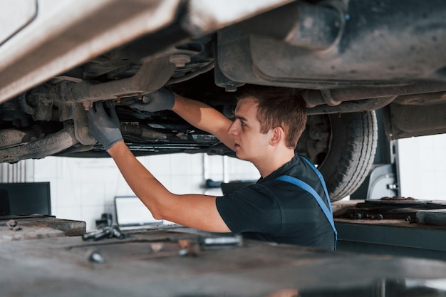 Il riparatore professionista in camicia nera lavora sotto l'automobile rotta