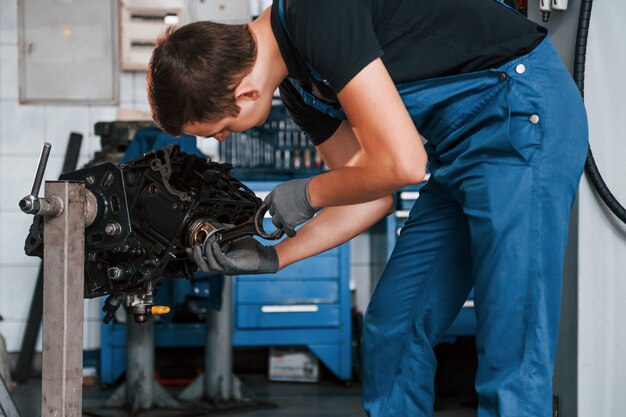 Il riparatore professionista in garage lavora con il motore di automobile rotto