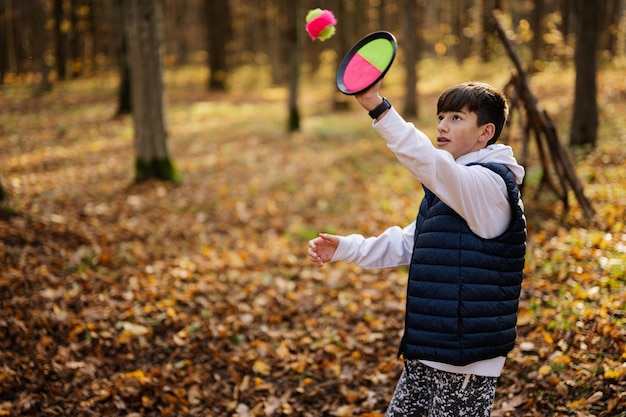 Il ritratto all'aperto di autunno del ragazzo gioca con il gioco della palla di cattura e lancio