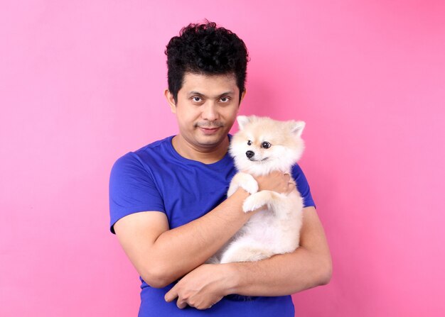 Il ritratto degli uomini asiatici tiene il cane pomeranian con amore e giocando con lui sul rosa una parete.