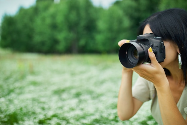 Il ritratto del fotografo femminile prende la foto all'aperto sul paesaggio del giacimento di fiore che tiene una macchina fotografica, macchina fotografica digitale della tenuta della donna nelle sue mani. Fotografia naturalistica di viaggio, spazio per il testo, vista dall'alto.