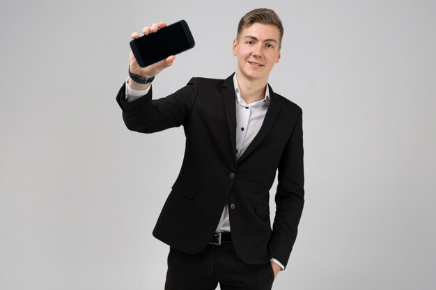 Il ritratto del giovane in vestito nero mostra il telefono cellulare con bianco isolato schermo in bianco