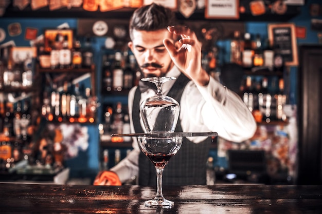 Il ritratto del mixologist mostra il processo di preparazione di un cocktail stando in piedi vicino al bancone del bar in discoteca
