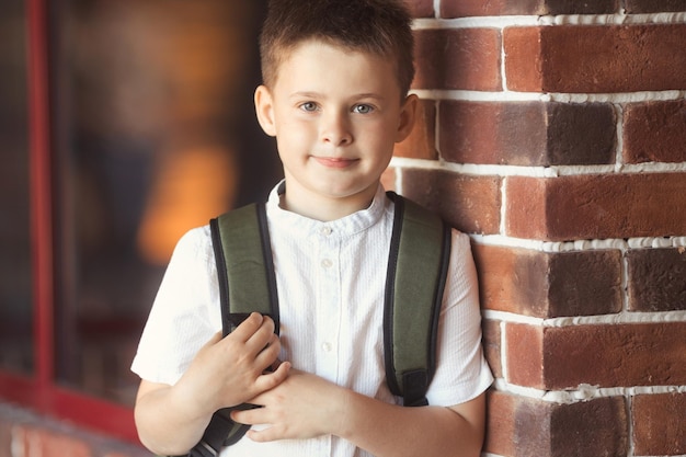 Il ritratto del primo piano del ragazzino sorridente di 7 anni va a scuola in uniforme e zaino