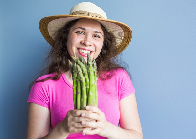 Il ritratto del primo piano della donna sorpresa divertente sta tenendo gli asparagi davanti al suo viso