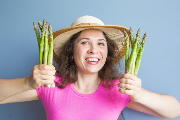 Il ritratto del primo piano della donna sorpresa divertente sta tenendo gli asparagi davanti al suo viso