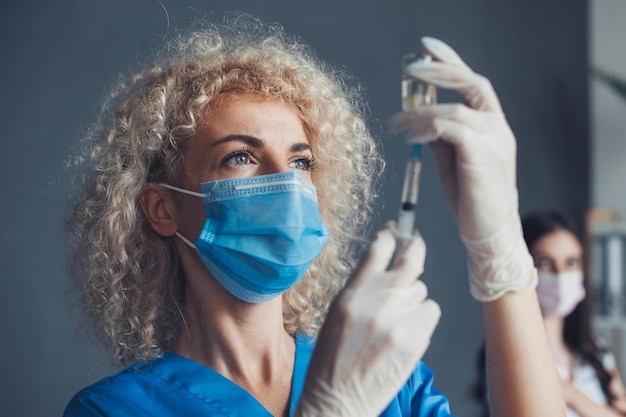 Il ritratto del primo piano di un'infermiera compone il vaccino in una siringa in ospedale donna dai capelli ricci salute m...