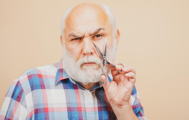 Il ritratto dell'uomo alla moda con la barba con i baffi grigi tiene le forbici da barbiere vicino al viso