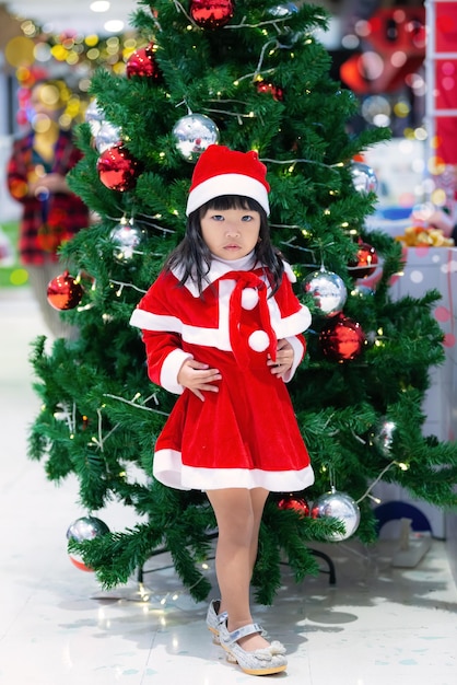 Il ritratto della bambina asiatica sveglia indossa il vestito da Babbo Natale felice vicino all'albero di natale Il bambino della Tailandia si unisce al festival di natale