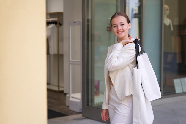 Il ritratto della bella donna teenager dell'adolescente teenager della ragazza alla moda positiva felice sta sorridendo divertendosi nel centro commerciale durante lo shopping che tiene in mano i sacchetti di carta della spesa