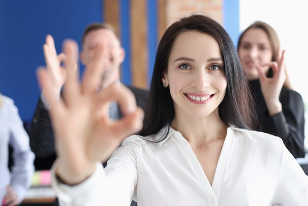 Il ritratto della donna d'affari dimostra il gesto ok sullo sfondo dei colleghi di lavoro