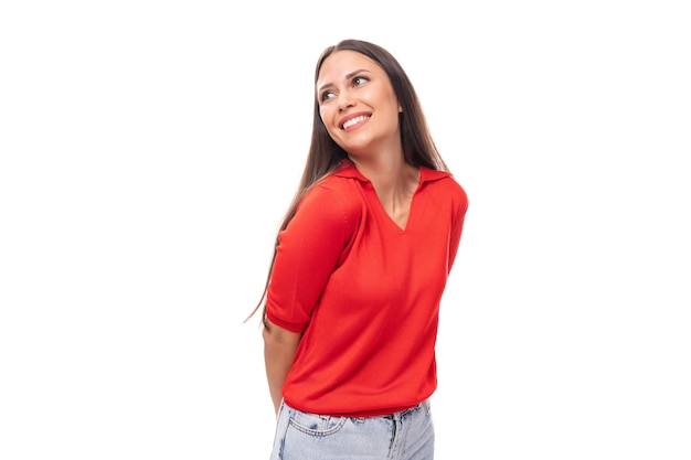 Il ritratto della donna graziosa castana sorridente con capelli lisci in maglietta rossa e jeans ha isolato lo studio