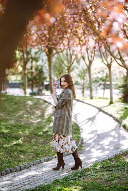 Il ritratto della donna in un vestito grazioso con i fiori gode di di fiorire giardino verde nel giorno di primavera. Concetto di moda e stile.