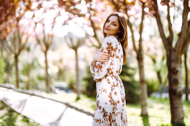 Il ritratto della donna in un vestito grazioso con i fiori gode di di fiorire giardino verde nel giorno di primavera. Concetto di moda e stile.