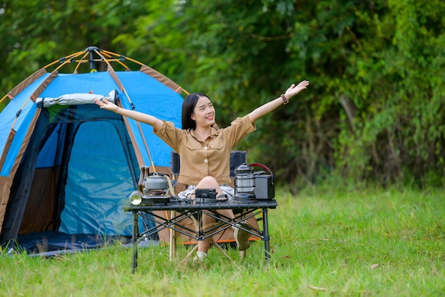 Il ritratto della giovane donna asiatica felice che si accampa da solo con il braccio aperto si siede davanti alla sua tenda in campeggio