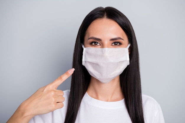 Il ritratto della maschera medica del punto del promotore della ragazza fiduciosa indica la nuova protezione di sicurezza covid29 che indossa un vestito di stile casual isolato su sfondo di colore grigio