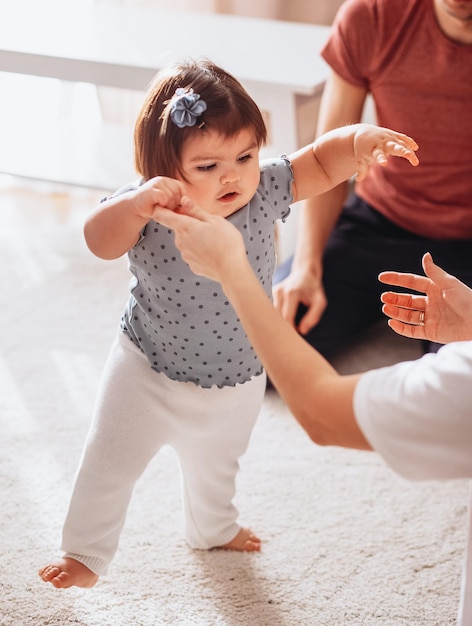 Il ritratto della piccola neonata sveglia impara a camminare a casa tenendo le mani della mamma piccolo infante cap