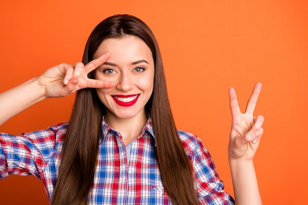 Il ritratto della ragazza adorabile affascinante gode del tempo libero del fine settimana di primavera fa l'espressione del viso di vsign indossare un vestito a scacchi isolato su uno sfondo di colore brillante