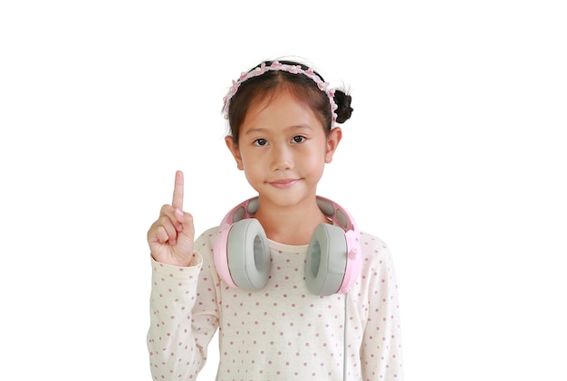 Il ritratto della ragazza asiatica del bambino con le cuffie sul collo mostra un indice isolato su fondo bianco.