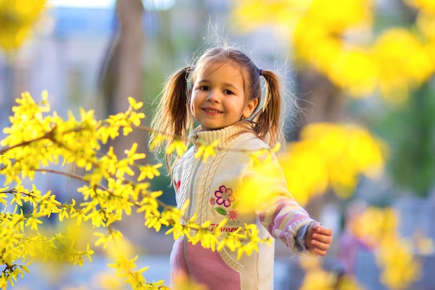 Il ritratto della ragazza con due code sulla passeggiata tra i cespugli fioriti di primavera gialla