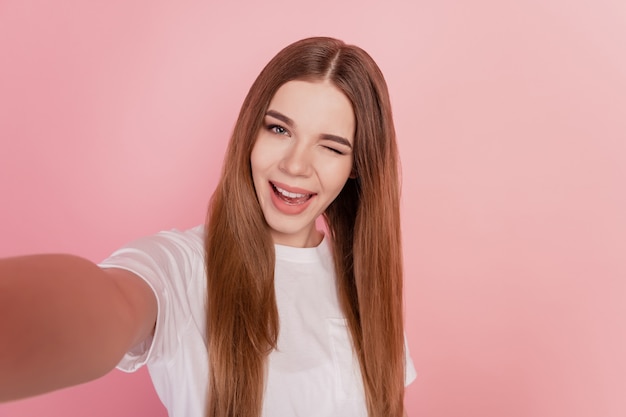 Il ritratto della ragazza graziosa prende il selfie su fondo rosa