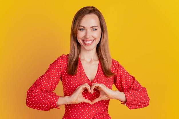 Il ritratto della signora affascinante ha formato una figura del cuore con le mani su fondo giallo