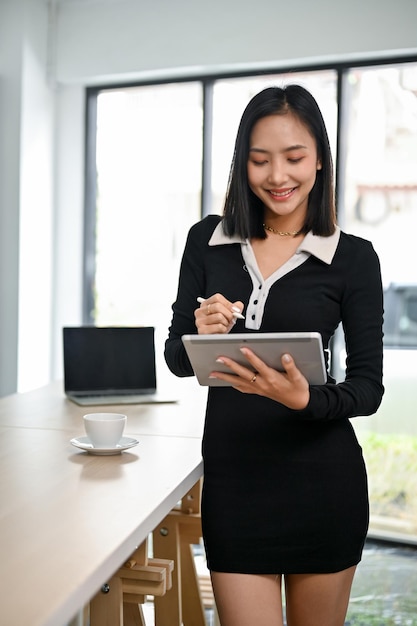 Il ritratto della splendida donna d'affari asiatica si trova nel suo ufficio e usa il suo tablet