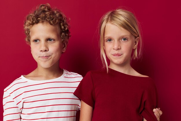 Il ritratto delle emozioni dei bambini carini sta fianco a fianco nei vestiti di tutti i giorni su sfondo rosso