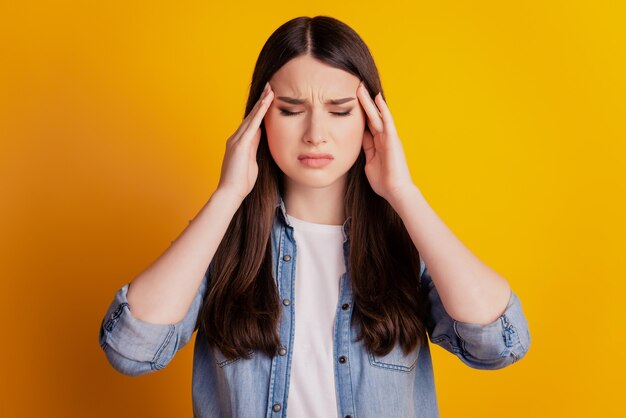 Il ritratto delle tempie delle dita stanche della donna ha l'emicrania su fondo giallo