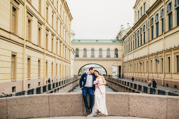 Il ritratto dello sposo e della sposa belli si abbracciano seduti sul ponte antico godono della calma e dello stare insieme hanno un buon rapporto Celebrazione del matrimonio e concetto di matrimonio