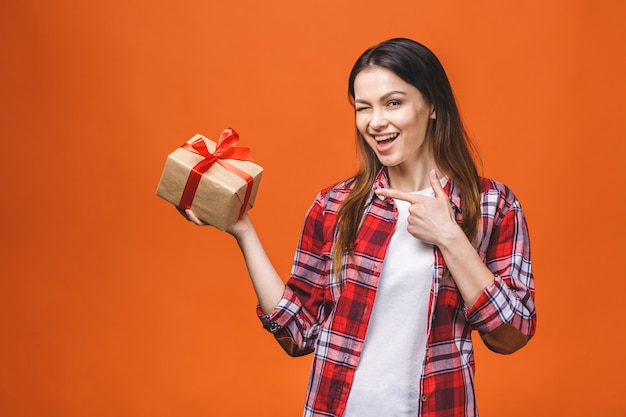 Il ritratto dello studio della giovane donna sorridente tiene il contenitore di regalo rosso. Isolato su sfondo arancione.