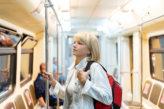 Il ritratto di bella donna adulta con lo zaino sta nella metropolitana e guarda avanti