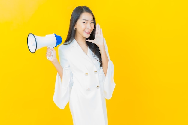Il ritratto di bella giovane donna asiatica sorride con il megafono sulla parete gialla
