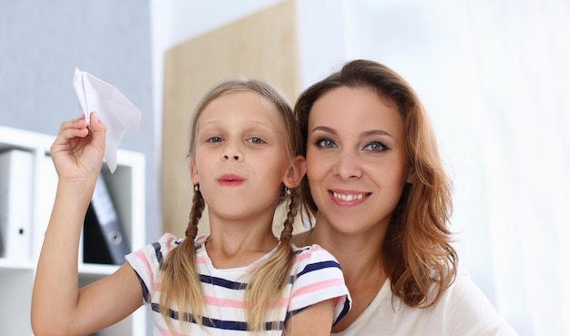 Il ritratto di bella mamma felice con la figlia sta tenendo l'aeroplano di carta