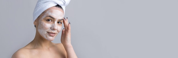 Il ritratto di bellezza della donna con un asciugamano bianco sulla testa applica la crema sul viso Detergente per la cura della pelle eco-cosmetico biologico spa relax concetto
