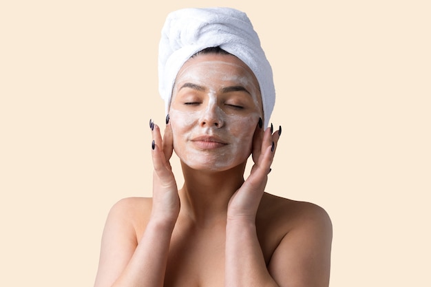 Il ritratto di bellezza della donna in asciugamano bianco sulla testa applica la crema al viso. Cura della pelle pulizia eco cosmetici biologici spa relax concetto.