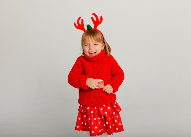 Il ritratto di Capodanno di una bambina in una cornice di cervo e un maglione rosso su sfondo bianco.