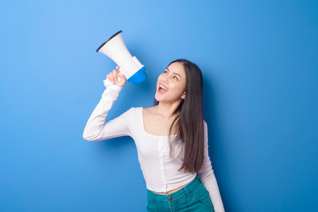 Il ritratto di giovane bella donna sorridente sta usando il megafono per annunciare sopra l'azzurro isolato