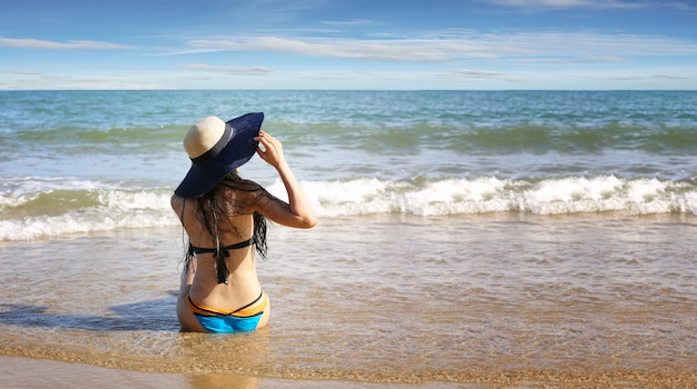 Il ritratto di giovane donna in bikini sulla spiaggia tropicale distoglie lo sguardo.