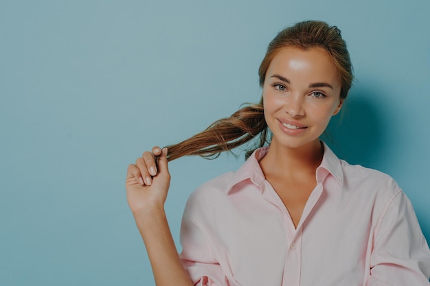 Il ritratto di giovane modello femminile attraente con capelli pettinati tiene delicatamente i sorrisi della coda di cavallo