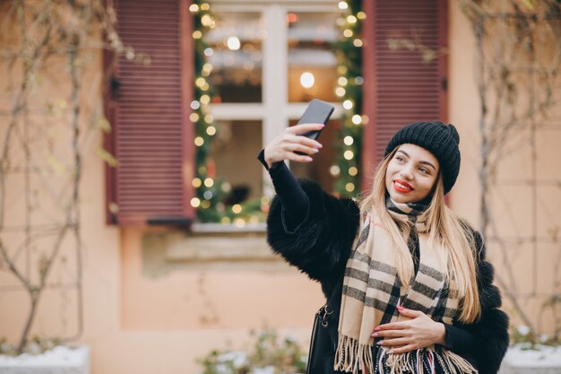 Il ritratto di inverno d'uso della giovane donna felice copre la presa del selfie