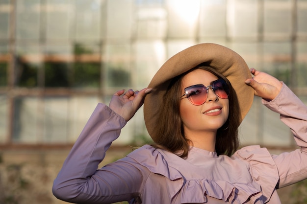 Il ritratto di strada di una donna bruna allegra indossa cappello e occhiali da sole, godendosi il clima caldo. Spazio per il testo