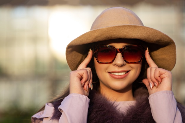 Il ritratto di strada di una donna bruna positiva indossa cappello e occhiali da sole, godendosi il clima caldo. Spazio per il testo