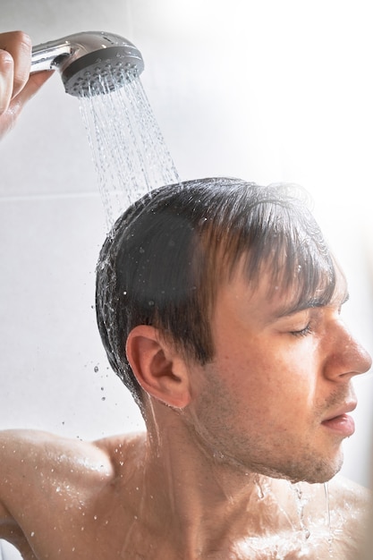 Il ritratto di un giovane bell'uomo si lava con il gel doccia, si insapona la testa con lo shampoo nel bagno di casa primo piano