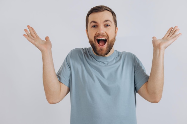 Il ritratto di un moderno uomo di mezza età con la barba in una maglietta blu mostra che non conosce l'emozione su uno sfondo bianco